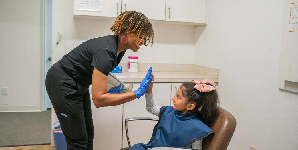 LaTonya, dental assistant at Sunnyvale Kids Pediatric Dentistry, high-fiving a pediatric dental patient